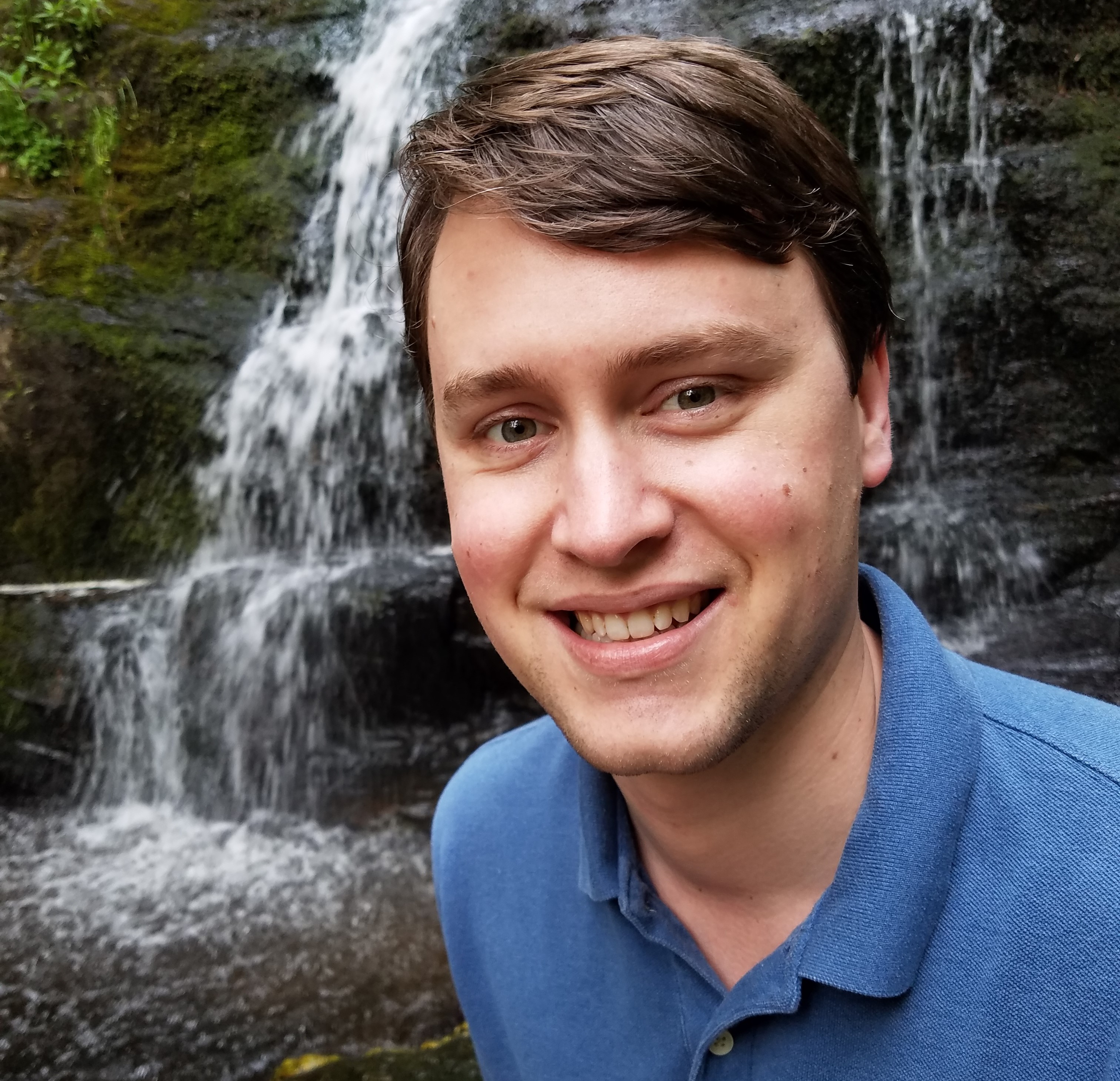 Portrait of the developer in a blue shirt by a waterfall.